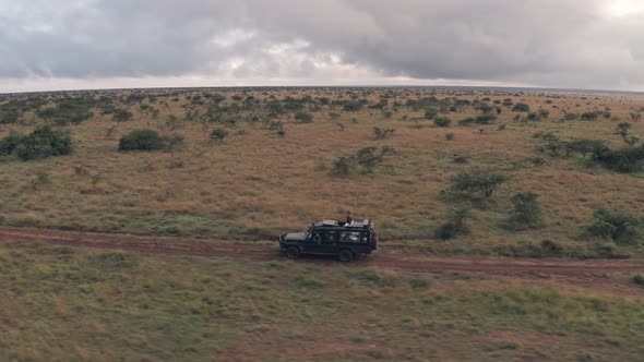 Woman sitting on top of 4 wheel drive while on wildlife safari holiday in Kenya. Aerial drone view