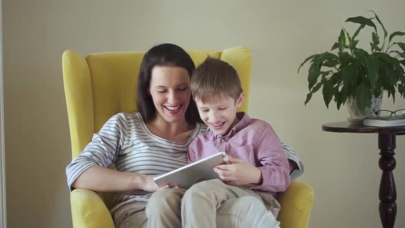 Caucasian Woman and Child Using Digital Gadget While Sitting on Chair in Apartment Room Spbd