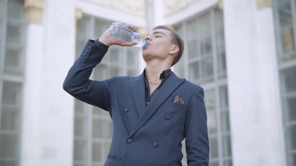 Middle Shot Portrait of Handsome Man Drinking Water From Bottle and Looking at Camera