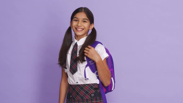 Happy Indian School Girl Wearing Uniform Holding Backpack on Lilac Background