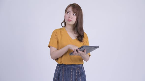 Happy Young Beautiful Asian Woman Thinking While Using Digital Tablet