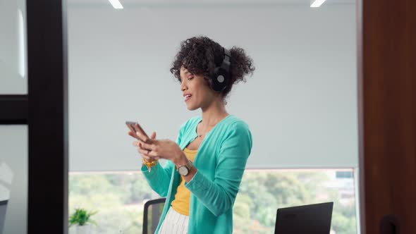 Young Black Woman Wearing Headphones Dancing And Singing in Office