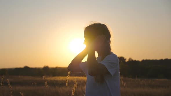 Portrait of Little Smiling Girl Look Into Camera Standing in Grass Field with Sunset at Background