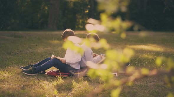 Schoolmates Sit Back To Back Preparing for Exams in Garden