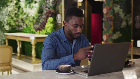 African american businessman using laptop and smartphone in cafe