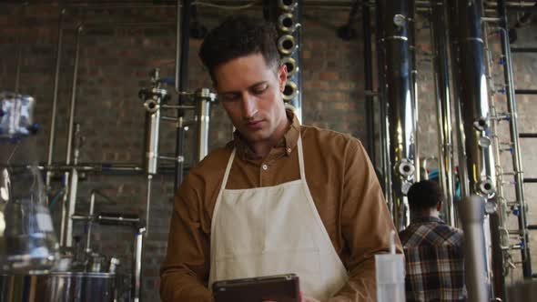 Caucasian man working at gin distillery, using digital tablet, wearing apron