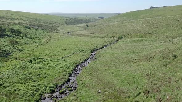 Wide aerial tracking forward slowly over a moorland river valley near Wistman's Wood. Dartmoor, Engl