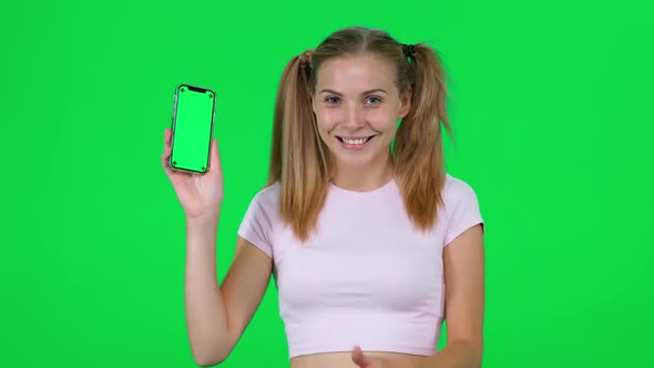 Cheerful Caucasian Female Holds a Smartphone in Her Hands and Shows It to the Camera Beautiful