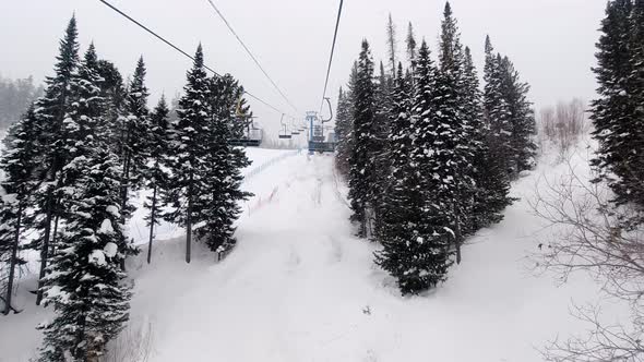 POV Empty Ski Chairlift Cableway Slowly Moves Above the Slopes in Snowy Weather