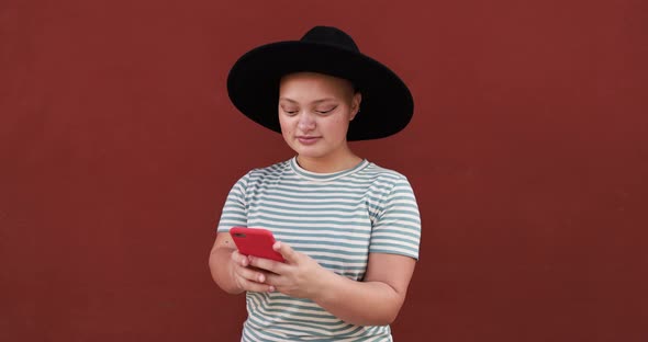 Bald young woman using mobile phone outdoor while wearing trendy hat