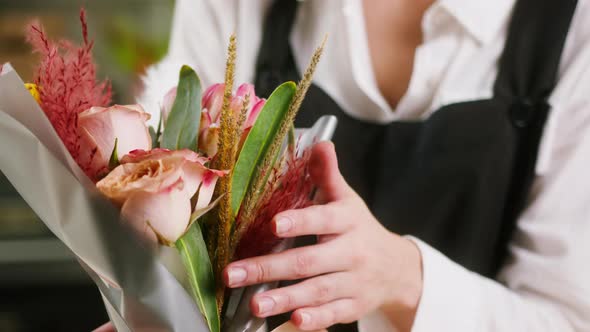 Young Florist Touching Wrapped Bouquet of Roses and Dried Flowers in Packaging Paper at Workplace