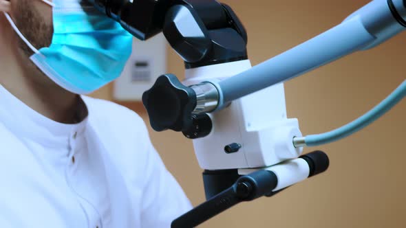 A male dentist looks into a microscope. Modern dentistry using new technologies.