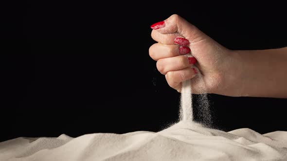 Female Hand Spilling a Handful of White Dry Sand Forming Hill on Isolated Black Studio Background