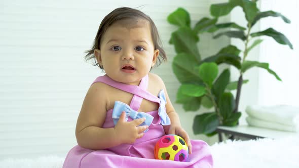 Adorable caucasian baby girl in pink clothes sitting on bed at home, playing toy color ball