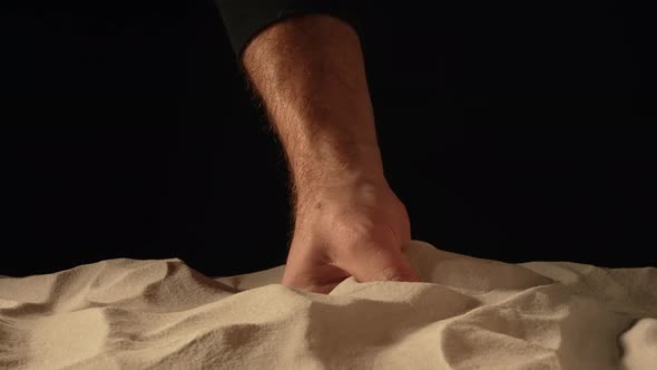 Man with Handful of White Dry Sand in Her Hands Spilling Sand Through Her Fingers on Black Studio