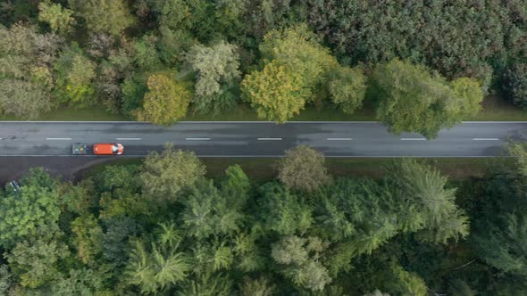 Top down view at a driving transporter at a road framed by autumn colored natural trees, concept for