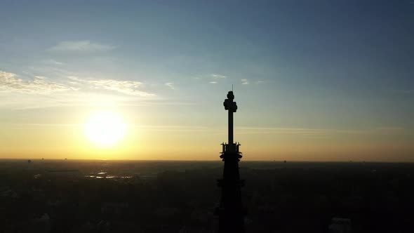 An aerial shot of a cathedral's steeple with a cross on top, taken at sunrise. The camera truck righ
