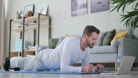 Man with Laptop Doing Plank on Yoga Mat at Home