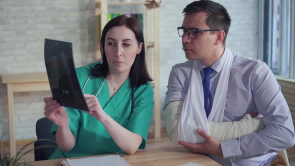 Woman Doctor with an Xray in Her Hand Communicates with a Patient with a Broken Arm