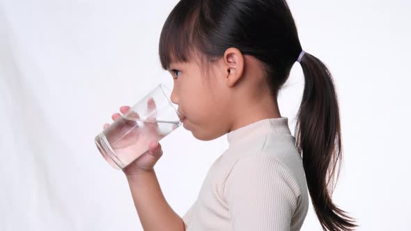 Cute little asian girl drinking water from a glass on white background in studio.