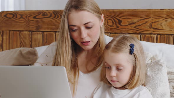 Portrait of Young Mother Adult Mum with Little Daughter Girl Child Look at Laptop Screen Talk in Web