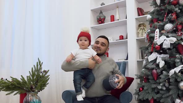 Handsome Man Holding in His Hands Funny Little Baby and Showing Him Beautiful Present 