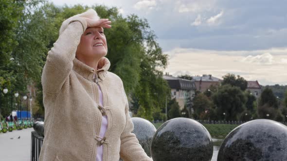 Attractive Elderly Woman Puts Hand to Forehead Covering Eyes From Bright Sunlight Peering Into