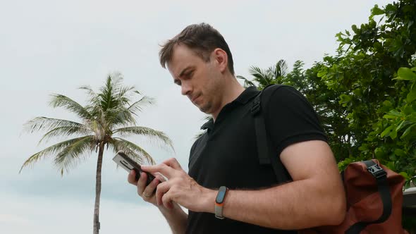 Travel Man Walking on Beach Resort with Backpack Looking on Mobile Phone