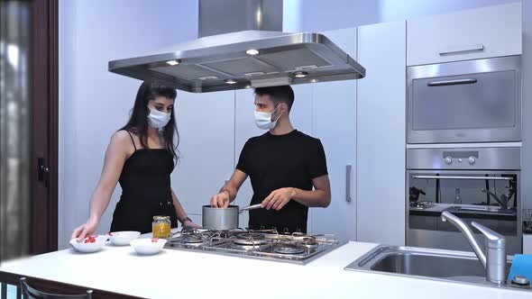 Couple in protective masks prepare food in the kitchen at their home.
