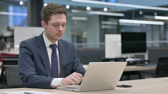 Businessman Looking at Camera While Using Laptop in Office