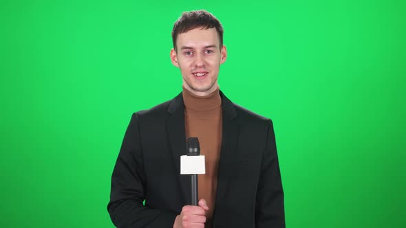 Man Reporter in Suit Looks Into the Camera and Speaks Into a Microphone on a Green Background a