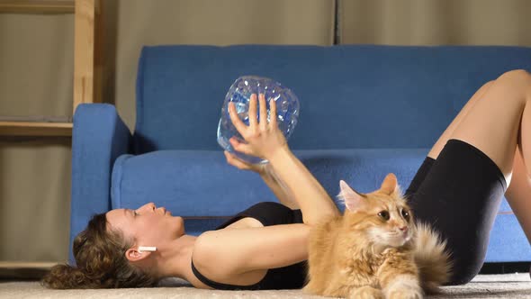 Lady Lifts Up Large Bottle with Water Near Cat on Floor