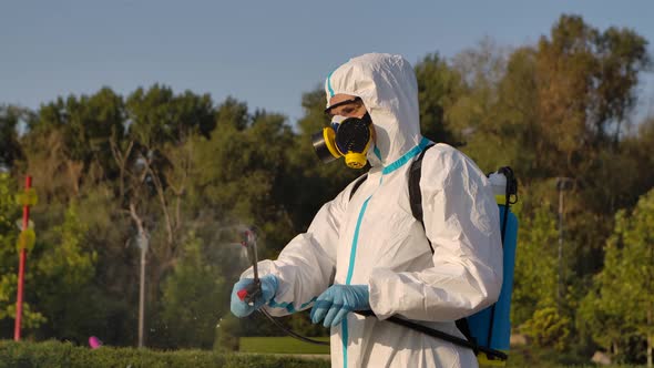 Side View of a Worker Disinfecting Outdoors in a Public Park with a Spray of Antibacterial