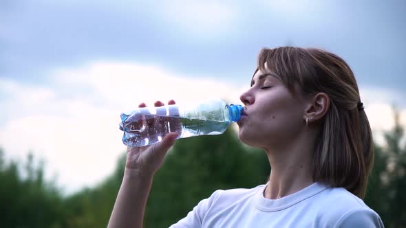 Young Beautiful Athletic Girl in a White T-shirt Is Very Tired and Drinks Water From a Transparent