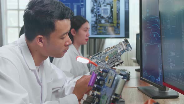 Asian Male Engineer Inspects Printed Circuit Board Motherboard. Scientist Designs Industrial Pcb