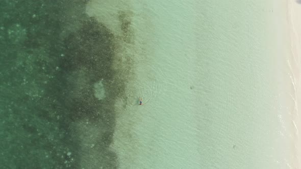 Aerial top down: Woman swimming in turquoise water tropical sea Indonesia