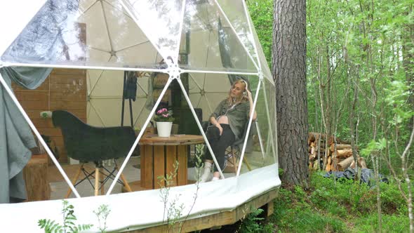 pregnant woman in headphones sits in a glamping tent in the forest