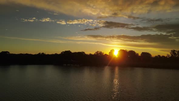 A dynamic aerial footage of a sunset with sun glares running through the trees while flying over a r