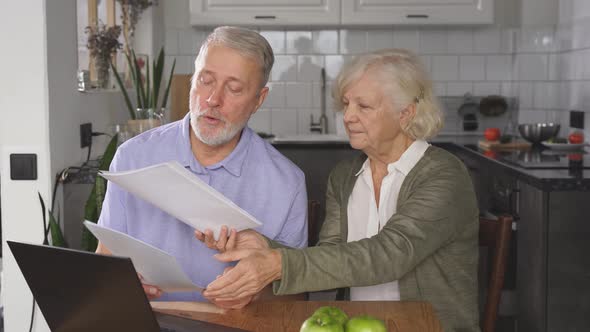 Elderly Couple Sits at a Desk and Uses a Laptop To Pay Bills