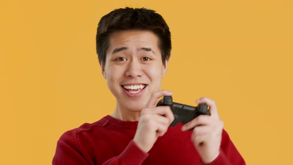 Joyful Asian Guy Playing Videogame Celebrating Victory Over Yellow Background