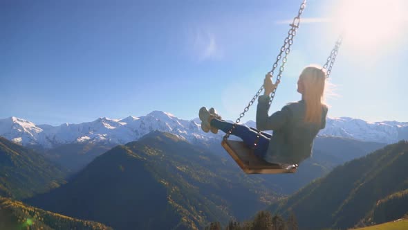 woman rides on large swing against background of mountains in Georgia,