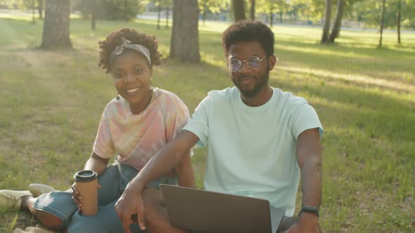 Portrait of Positive Afro Man and Woman Sitting on Grass in Park