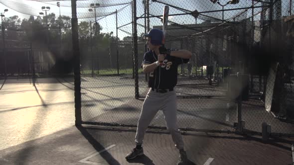 A young man practicing baseball at the batting cages.