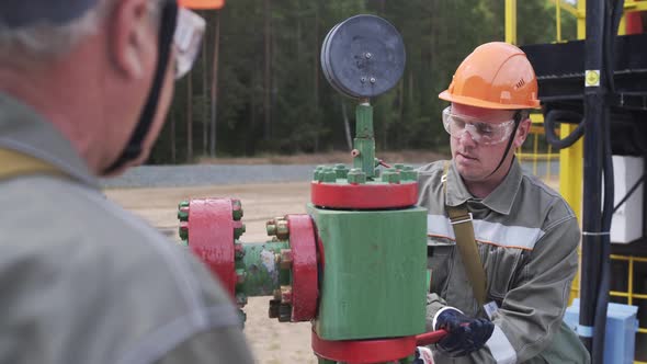 Oilman in Orange Helmet and Protective Glass Closing Valve of X-mass Wellhead To Shut Off Well
