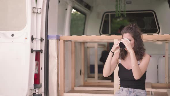 Cute woman drinking fresh coffee during camper trip in own caravan,close up