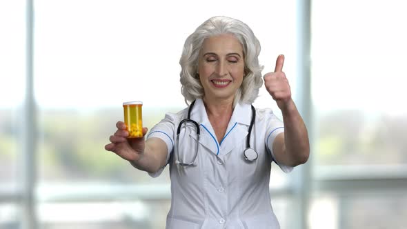 Old Cheerful Female Doctor Advertising Yellow Bottle of Medicine