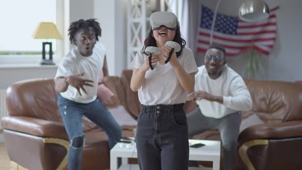 Young Smiling Asian Woman in VR Headset Boxing in Augmented Reality As African American Men Cheering