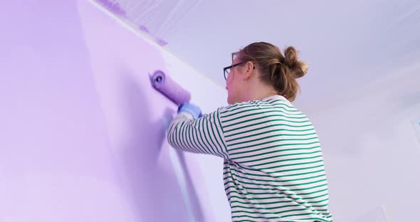 Curvy Blonde Woman Paints Top of Wall Purple Using Roller