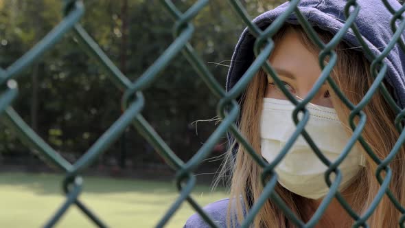 Closed Border. Quarantine. Close-up of Young Woman Wearing Protective Face Mask Stand Behind Fence