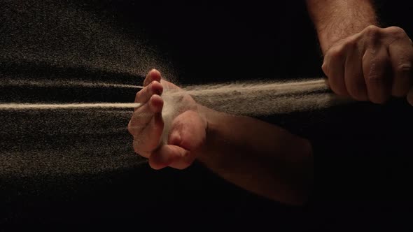 Stream of Dry Sand Pours Into Palm of Man and is Spilling Through His Fingers on Black Background